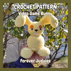 May include: Crochet pattern for a yellow video game bunny. The bunny has a black nose, orange eyes, and a white mouth. The pattern is available on Etsy from the shop Forever Judalee.