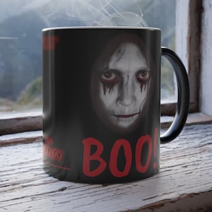 May include: Black coffee mug with a spooky face and the word "BOO!" in red letters. Steam is rising from the mug.