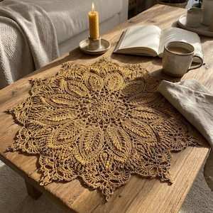 以下が含まれることがあります： 木製のコーヒーテーブルの上に、金色の黄色の花の模様の編み物コースターがあります。 ろうそく、本、コーヒーカップもテーブルにあります。 コースターの複雑なパターンは、装飾的なタッチを追加します。
