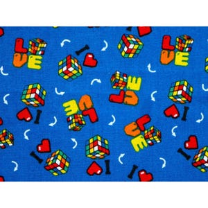 Puede incluir: Tela azul con un patrón repetido de cubos de Rubik coloridos, corazones rojos y las palabras "LOVE" e "I". El diseño incluye líneas curvas blancas y símbolos "I" negros. Los cubos son de varios colores.