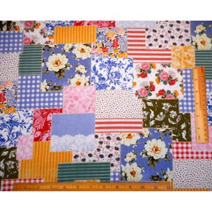 May include: A patchwork fabric with a variety of floral, striped, and patterned squares in shades of blue, pink, red, and yellow. A wooden ruler is placed along the bottom edge, measuring in inches.