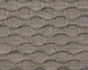 May include: A taupe fabric featuring a repeating geometric pattern of raised, rounded, chain-link shapes. The texture is created by a dense weave with a visible grid structure, alternating between smooth flat sections and textured, fuzzy raised loops.