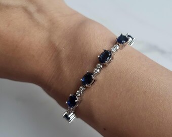 May include: A silver bracelet featuring oval-cut, dark blue gemstones and small, round, clear stones. The bracelet is designed with a linked chain and is worn on a wrist. The gemstones are set in a silver metal.