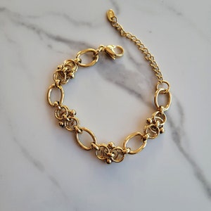 May include: Gold bracelet featuring oval and beaded links. The bracelet has an adjustable chain and a lobster clasp. The jewellery is displayed on a white marble surface.