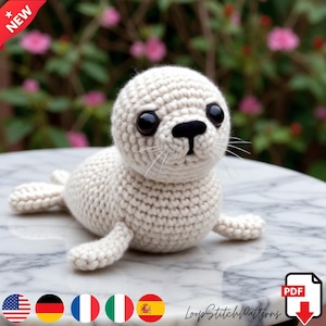 Puede incluir: Una foca de ganchillo hecha a mano, de color blanquecino, con ojos negros y nariz negra. La foca está tumbada sobre una superficie de mármol. La imagen incluye el texto "LoopStitchPatterns" y una pancarta "NEW".
