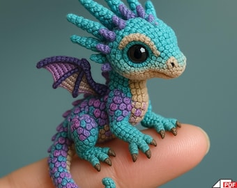 May include: A crocheted amigurumi dragon in shades of teal, purple, and tan. The dragon has large black eyes, small wings, and a spiky crest. The text "AMIGURUMI - PDF PATTERN" is at the top.