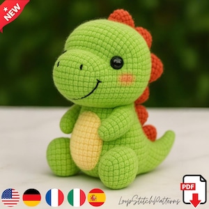 May include: A handmade green crochet dinosaur with orange spikes, a yellow belly, and black eyes. The dinosaur is smiling and has pink cheeks. The image includes the text "NEW" and "LoopStitchPatterns".