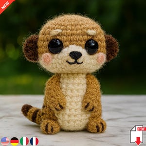 May include: A crocheted meerkat toy in brown and cream, with large black eyes and pink cheeks. The meerkat is sitting upright, with its tail curled to the side. The image has a blurred green background. A red "NEW" banner is in the top left corner.