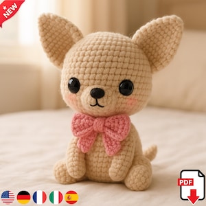 Pode incluir: Um cão chihuahua de crochê com grandes olhos pretos, bochechas rosadas e uma gravata borboleta rosa. O cão bege é feito à mão e tem orelhas grandes e caídas. O cão está sentado em posição vertical em uma superfície clara.