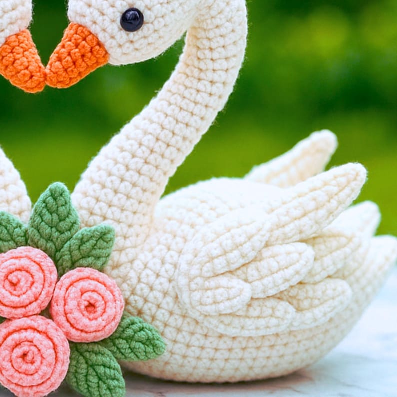 Romantic crochet swan sculpture featuring heart-shaped necks, tiny roses, and blushing cheeks, resting on a marble surface with a garden background.