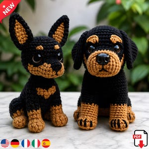 May include: Two crocheted dog figurines. One is a black and tan Chihuahua with large ears. The other is a black and tan Rottweiler. Both are sitting upright with large, round eyes. The Chihuahua has a heart-shaped tan marking on its chest.