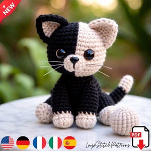 Op de afbeelding: Een handgemaakte gehaakte kat in zwart en crème kleuren. De kat heeft grote, glanzende ogen en lange snorharen. De kat zit, met zijn staart en poten zichtbaar. De afbeelding bevat de tekst "NEW" en "LoopStitchPatterns".
