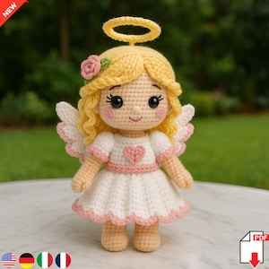 Könnte beinhalten: Eine gehäkelte Engels-Puppe mit Heiligenschein und Flügeln. Die Puppe hat blondes Haar, rosige Wangen und ein rosa Herz auf dem weißen Kleid mit rosa Besatz. Ein handgefertigter Artikel, ideal als Geschenk oder Dekoration.