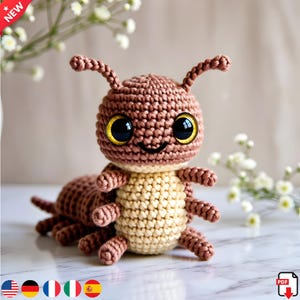 May include: A handmade crochet insect toy in shades of brown and beige. The toy has large, expressive eyes with yellow rims and a smiling mouth. The antennae and legs are detailed. The word "NEW" is in the upper left corner.