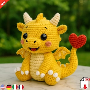 Puede incluir: Un dragón amarillo tejido a mano con una cola en forma de corazón rojo. El dragón tiene ojos negros, cuernos color crema y mejillas rosadas. Está sentado con las alas extendidas. Un juguete artesanal y encantador.