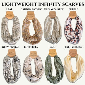 May include: Eight infinity scarves in various colors and patterns, including leaf, garden mosaic, cream paisley, purple, grey floral, butterfly, sage, and pale yellow. Each scarf is labeled with the "Cozy Naturals Company" logo.