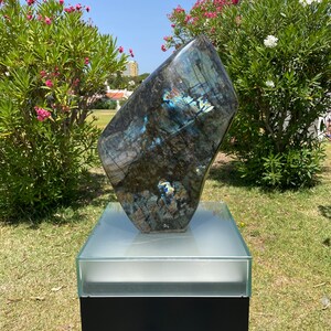 May include: A large, dark blue, iridescent, polished labradorite stone sculpture on a black pedestal with a glass top.