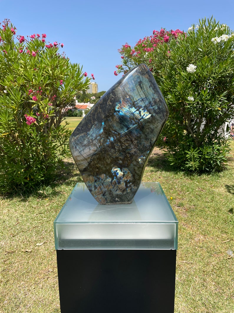 May include: A large, dark blue, iridescent, polished labradorite stone sculpture on a black pedestal with a glass top.