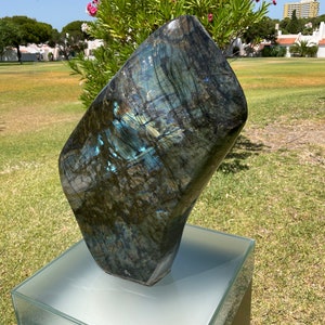May include: A large, dark blue and green labradorite gemstone sculpture on a white pedestal. The sculpture is smooth and polished, with a unique iridescent sheen.