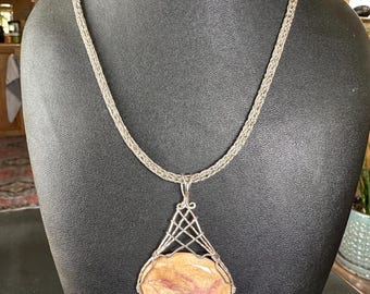 May include: A silver chain necklace with a pendant featuring a large, oval-shaped, multi-colored stone set in a silver wire cage.