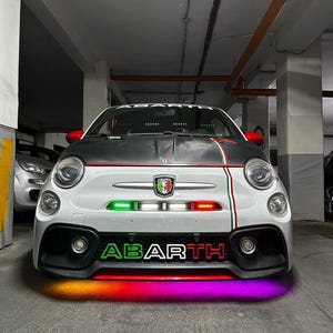 May include: A white Abarth car with a black hood and red accents. The car has green, white, and red stripes and a front bumper with the word "ABARTH" in green and red. The car's undercarriage is illuminated with a rainbow of colors.