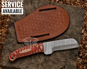May include: A Damascus steel knife with a red and white wood handle. The knife is sitting on a wooden surface with a brown leather sheath. The text "RAZOR EDGE KNIVES" is visible on the sheath.