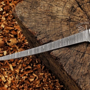 May include: A Damascus steel knife with a long, slender blade. The blade has a unique pattern and is set against a rustic wooden background. The knife's handle is white, and the text "RAZOR EDGE KNIVES" is visible.