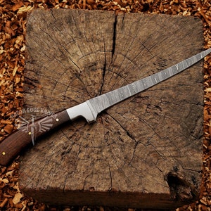 May include: A Damascus steel knife with a dark wood handle and a silver bolster rests on a wooden block. The blade has a distinctive pattern. The handle is secured with brass rivets. The logo "RAZOR EDGE KNIVES" is visible.
