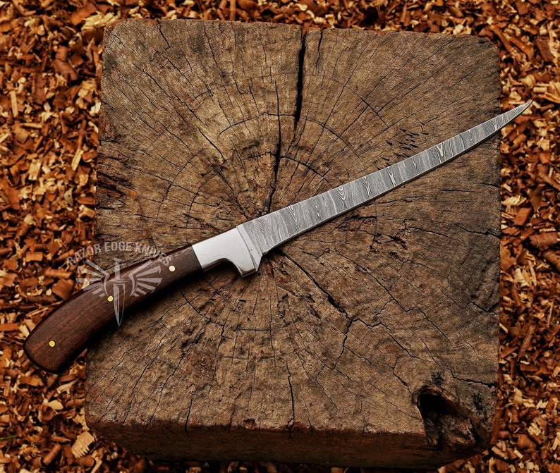 May include: A Damascus steel knife with a dark wood handle and a silver bolster rests on a wooden block. The blade has a distinctive pattern. The handle is secured with brass rivets. The logo "RAZOR EDGE KNIVES" is visible.