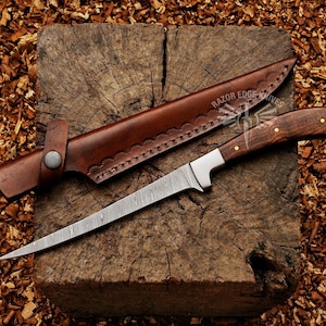 May include: A Damascus steel knife with a wooden handle and a brown leather sheath. The knife has a long, slender blade and is resting on a wooden block. The sheath is open, revealing the knife. The text "RAZOR EDGE KNIVES" is visible.