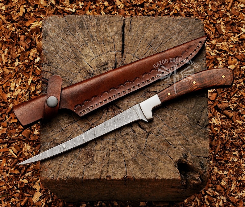 May include: A Damascus steel knife with a wooden handle and a brown leather sheath. The knife has a long, slender blade and is resting on a wooden block. The sheath is open, revealing the knife. The text "RAZOR EDGE KNIVES" is visible.
