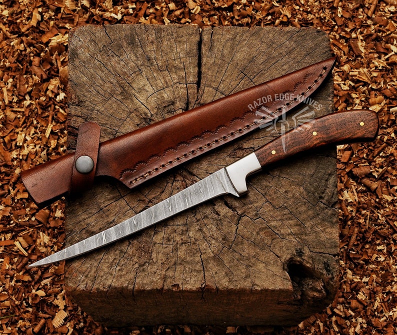 May include: A Damascus steel knife with a wooden handle and a brown leather sheath. The knife has a long, slender blade and is resting on a wooden block. The sheath is open, revealing the knife. The text "RAZOR EDGE KNIVES" is visible.