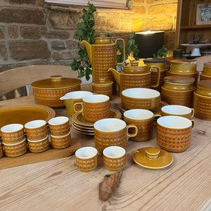 May include: A vintage brown and orange patterned tea set with a teapot, creamer, sugar bowl, cups, saucers, and a serving dish. The set is arranged on a wooden table.