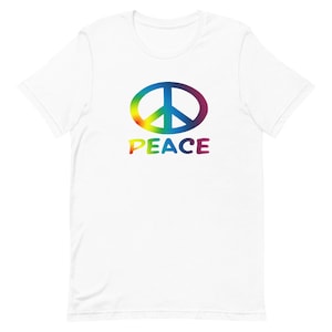 Puede incluir: Camiseta blanca con un símbolo de paz arcoíris y la palabra "PAZ" impresa en colores arcoíris.