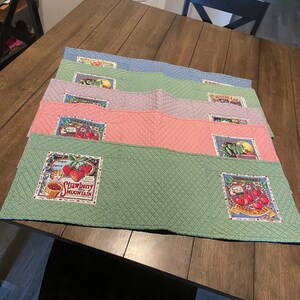 May include: Set of five quilted table runners with a vintage fruit design. The runners are in shades of green, blue, pink, and purple. Each runner features a different fruit design, including strawberries, cherries, and lemons. The runners are perfect for adding a touch of country charm to any dining table.