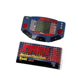 May include: A blue and red Jeopardy! handheld electronic game and a spiral-bound Answer/Question Book. The game has a screen, buttons, and the Jeopardy! logo. The book has the Jeopardy! logo and text.
