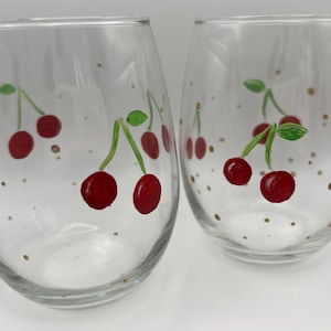 May include: Two clear glass wine glasses with hand-painted red cherries and gold dots.