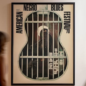Puede incluir: Póster enmarcado del Festival Americano de Blues Negro de 1970. El póster presenta una jaula en forma de guitarra con una figura dentro. El texto del póster incluye el nombre del festival y los nombres de los artistas. El póster está enmarcado en negro.