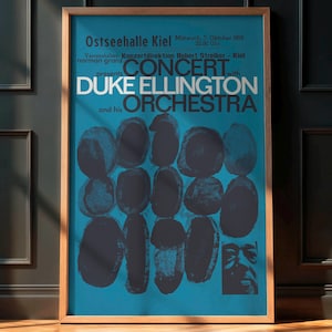Puede incluir: Cartel de concierto enmarcado con "Duke Ellington and his Orchestra". El cartel tiene un fondo turquesa con formas abstractas y texto en azul oscuro. El cartel está en un marco de madera y se exhibe contra una pared oscura.