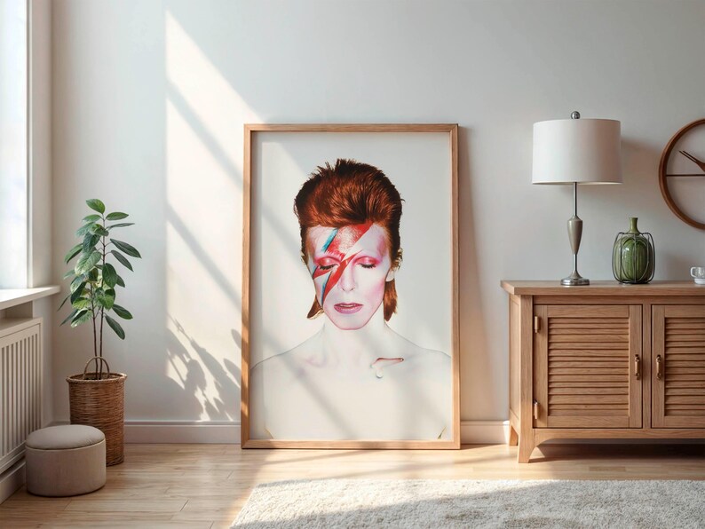 May include: A framed portrait of a person with red hair and a lightning bolt painted across their face. The artwork is displayed in a well-lit room with a wooden cabinet, a lamp, and a potted plant.