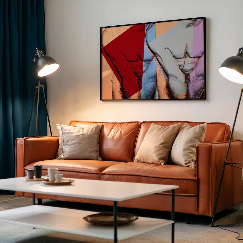 May include: A modern living room featuring a brown leather sofa with beige pillows, a white coffee table, and a framed artwork depicting a male torso in vibrant colors. Two black floor lamps flank the sofa.