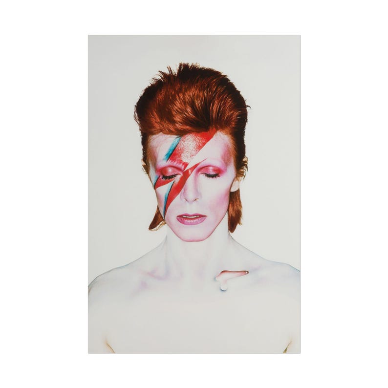 May include: A portrait of a person with red hair and a red and blue lightning bolt painted on their face. The person has closed eyes and a pale complexion. The background is a solid white.
