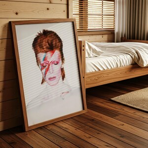May include: A framed portrait of a person with red hair and a lightning bolt painted across their face. The portrait is in a wooden frame and leans against a wooden wall. The person has closed eyes and a neutral expression.