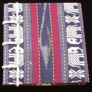 May include: A small, handmade notebook with a dark blue and red striped cover. The cover is decorated with a white pattern of elephants. The notebook is bound with white string.