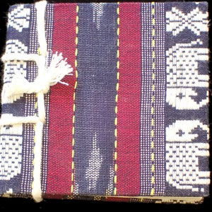 May include: A small, handmade notebook with a blue, red, and white striped cover. The cover is made of woven fabric and has a white tassel.