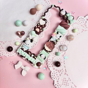 May include: A clear phone case decorated with a chocolate and mint theme. The case features a cartoon dog, chocolate bars, marshmallows, and sprinkles. The text "POCHACCO" is written on the case.