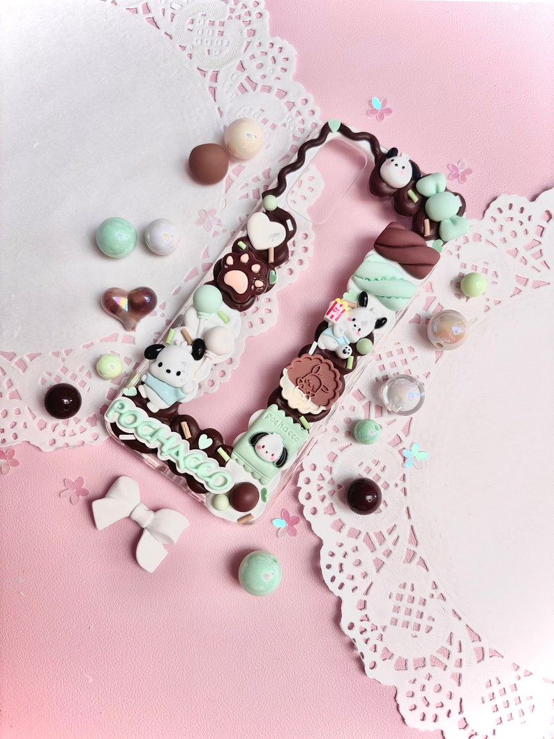 May include: A clear phone case decorated with a chocolate and mint theme. The case features a cartoon dog, chocolate bars, marshmallows, and sprinkles. The text "POCHACCO" is written on the case.