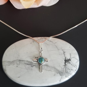 May include: A silver chain necklace with a turquoise stone cross pendant.