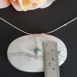May include: A silver chain necklace with a turquoise stone cross pendant. The pendant is approximately 2.5 cm in size and is shown next to a ruler for scale.