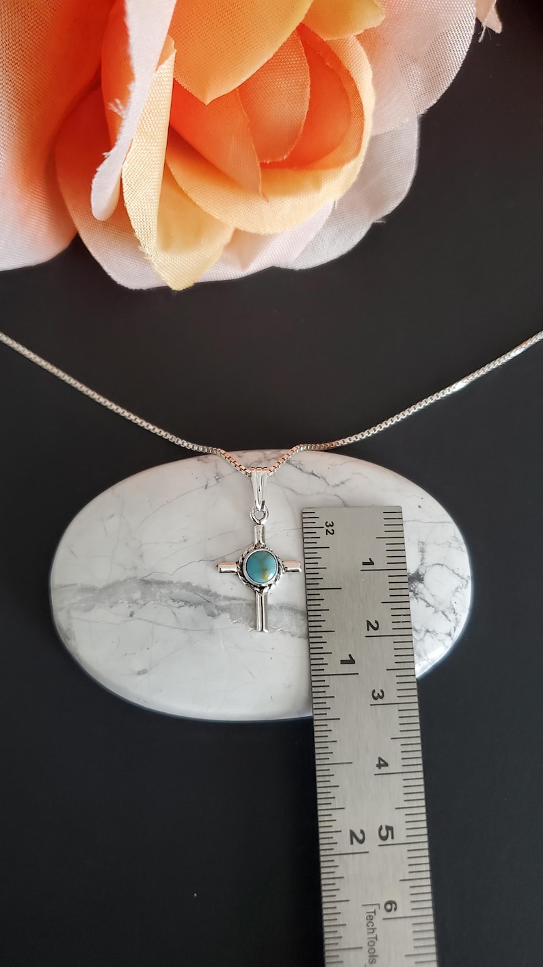 May include: A silver chain necklace with a turquoise stone cross pendant. The pendant is approximately 2.5 cm in size and is shown next to a ruler for scale.